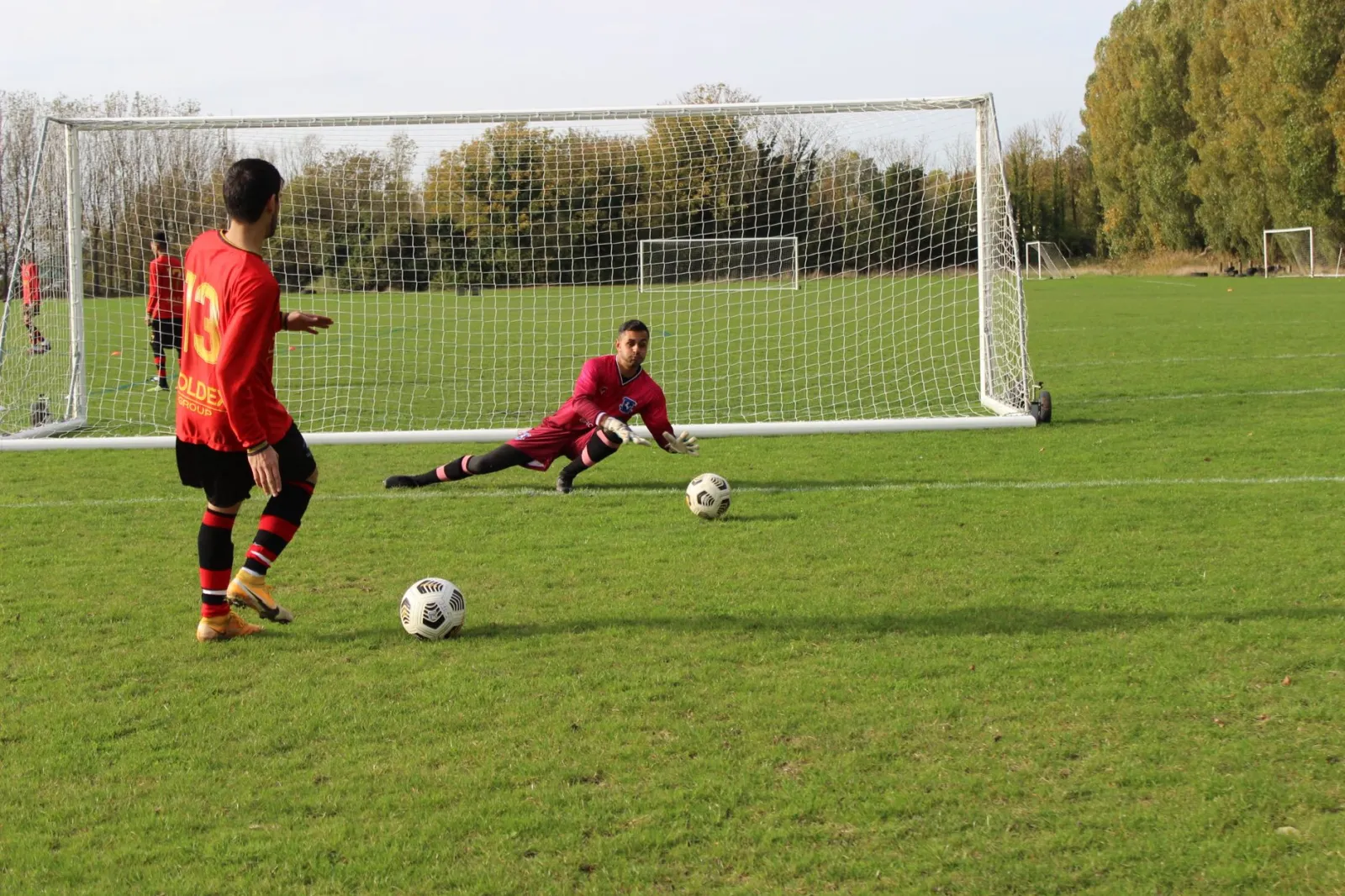 A soccer player prepares to take a shot as the goalkeeper dives to save in an outdoor match.